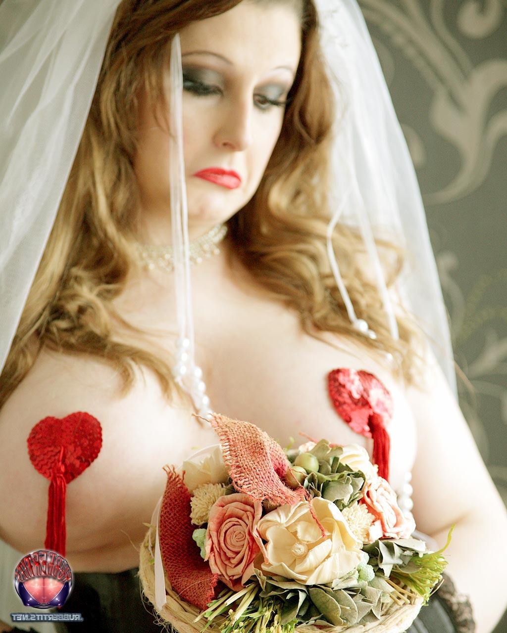 16P Une mariée rousse arbore des cache-tétons dans un corset en latex noir.