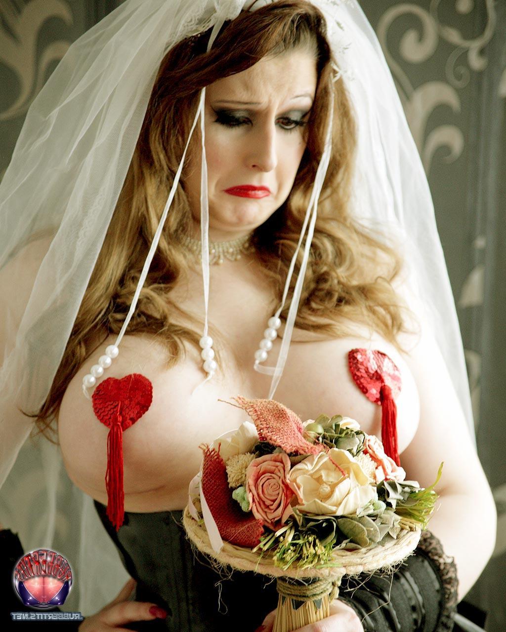 16P Une mariée rousse arbore des cache-tétons dans un corset en latex noir.
