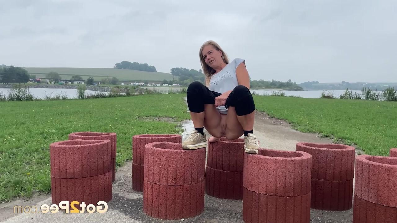 15P Das blonde Mädchen Juliia pinkelt auf zylinderförmige Geräte, die eine Straße blockieren