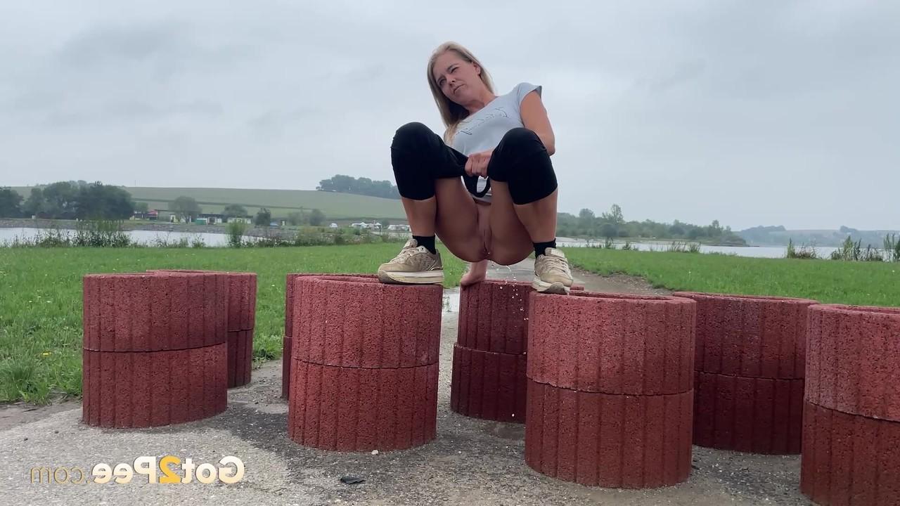 15P Das blonde Mädchen Juliia pinkelt auf zylinderförmige Geräte, die eine Straße blockieren