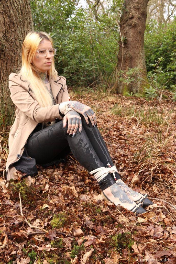 16P Eine Frau mit Brille ist mit Seilen an einen Baum im Wald gefesselt und trägt Kleidung