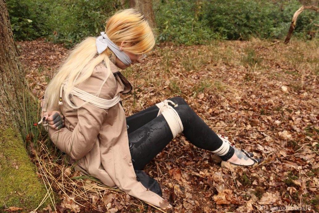 16P Eine Frau mit Brille ist mit Seilen an einen Baum im Wald gefesselt und trägt Kleidung