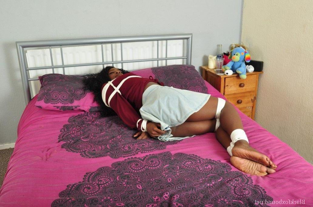16P Ebony female is tied up on a bed while gagged and fully clothed