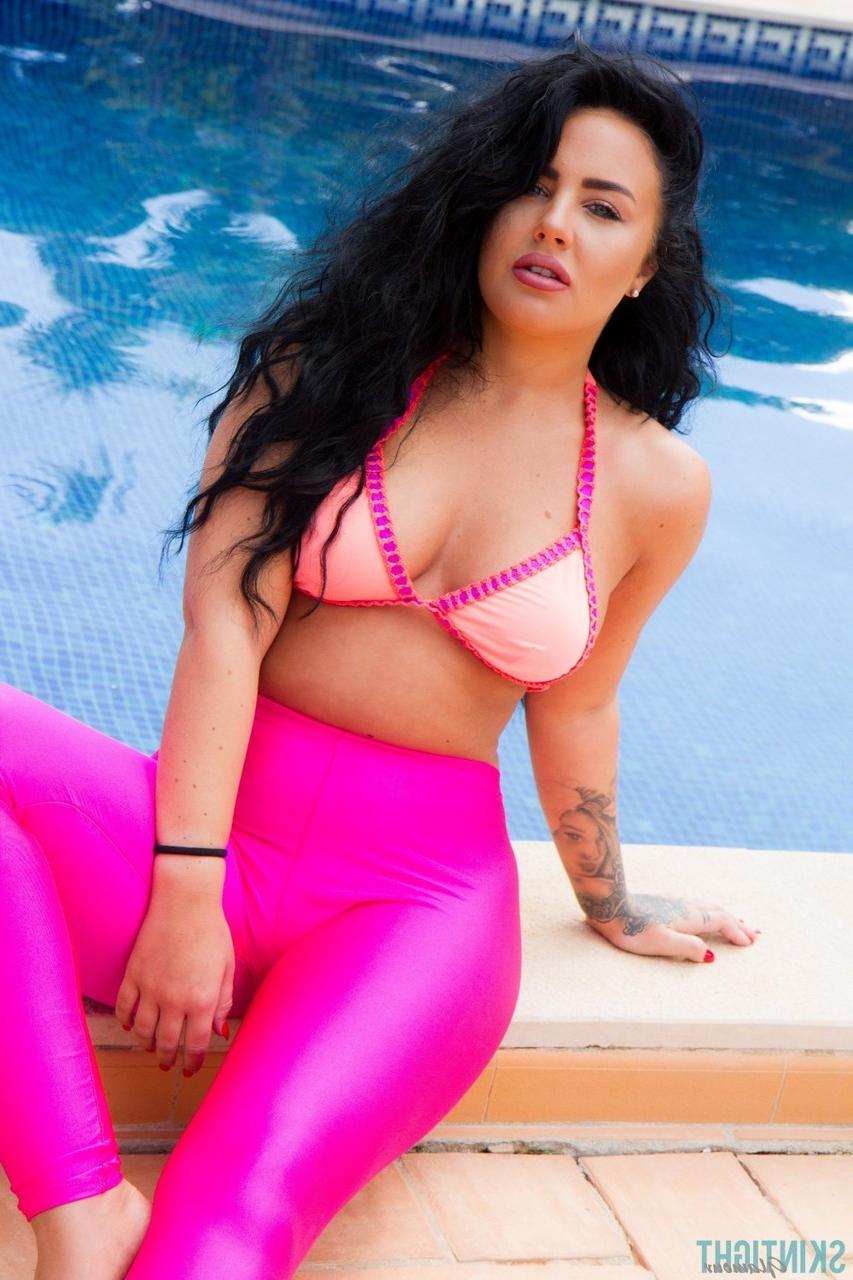 12P A modelo glamourosa Olivia Paige coloca leggings rosa sobre a parte de baixo do biquíni à beira da piscina