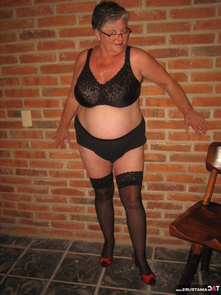 20P Fette alte Frau zieht sich bis auf ihre schwarzen Strümpfe und High Heels aus und trägt ihre Brille