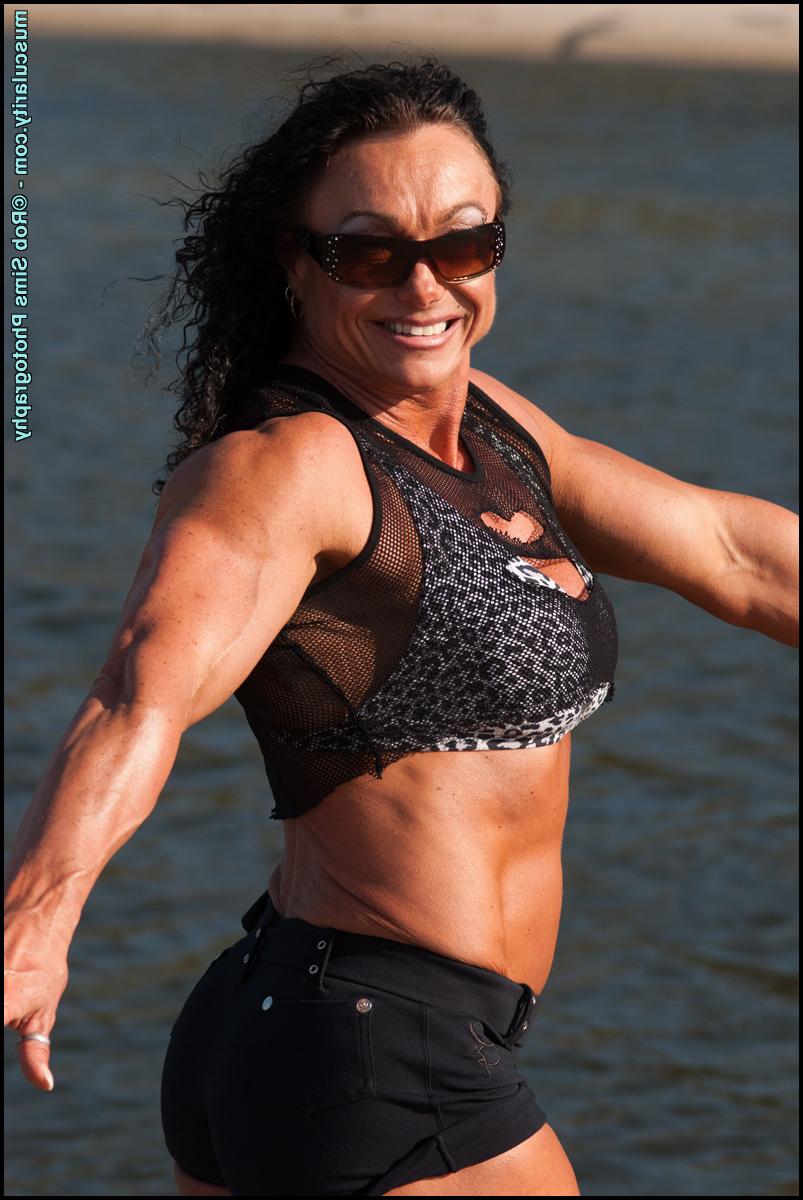 15P La culturista morena madura sharon mold se flexiona en una playa con gafas de sol