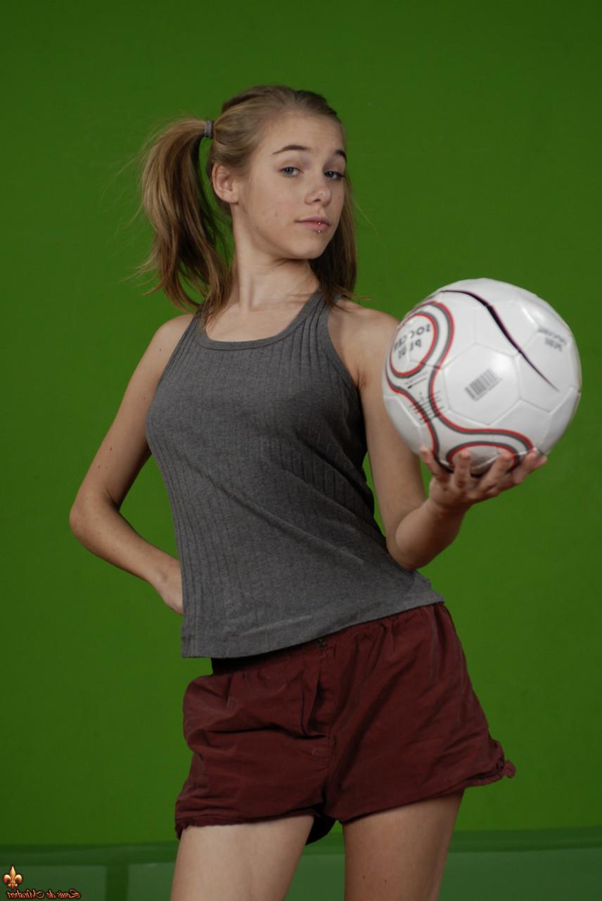 16P Das zierliche Mädchen Kelly entblößt ihre Brust, während sie einen Fußball hält