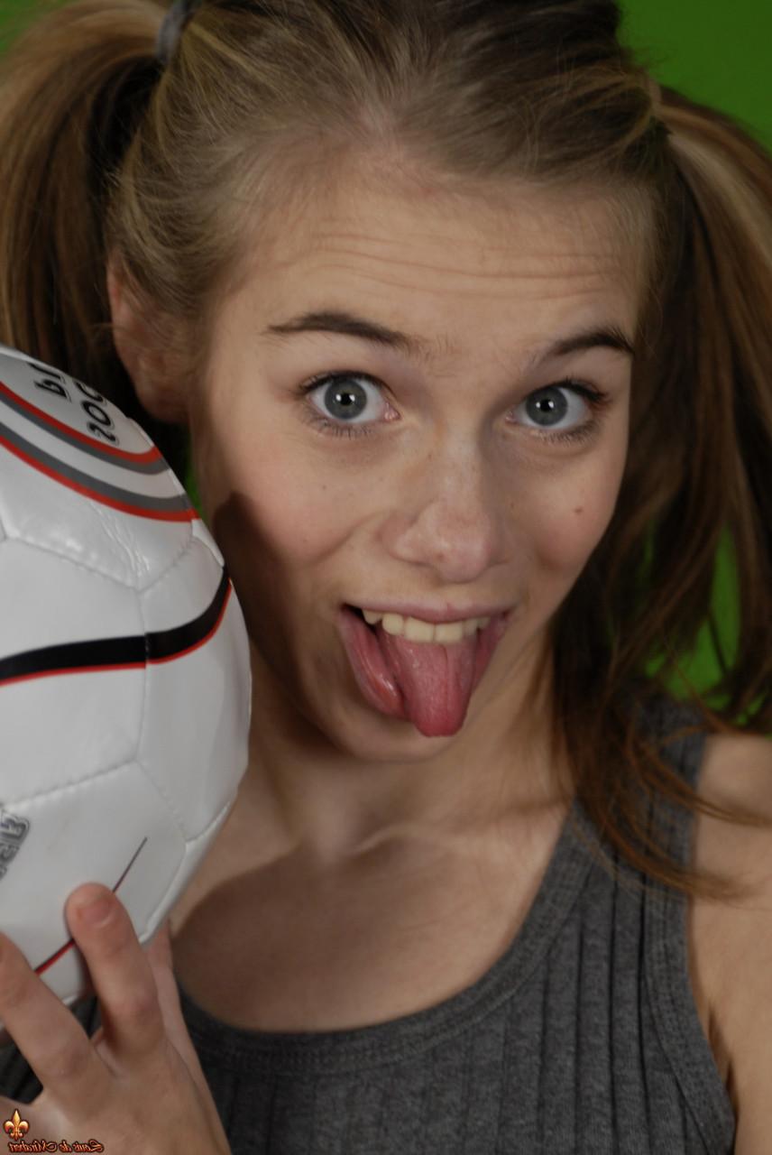 16P Das zierliche Mädchen Kelly entblößt ihre Brust, während sie einen Fußball hält