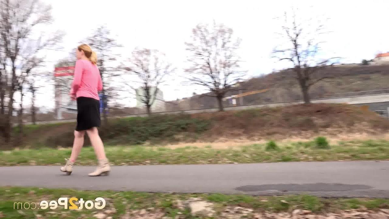 15P Mädchen mit erdbeerblonden Haaren zieht bei einer Mutprobe ihren Rock hoch, um auf dem Rasen zu pinkeln