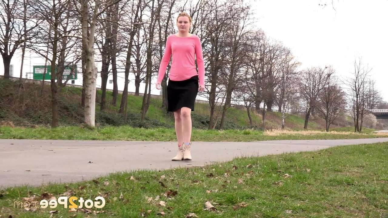 15P Mädchen mit erdbeerblonden Haaren zieht bei einer Mutprobe ihren Rock hoch, um auf dem Rasen zu pinkeln