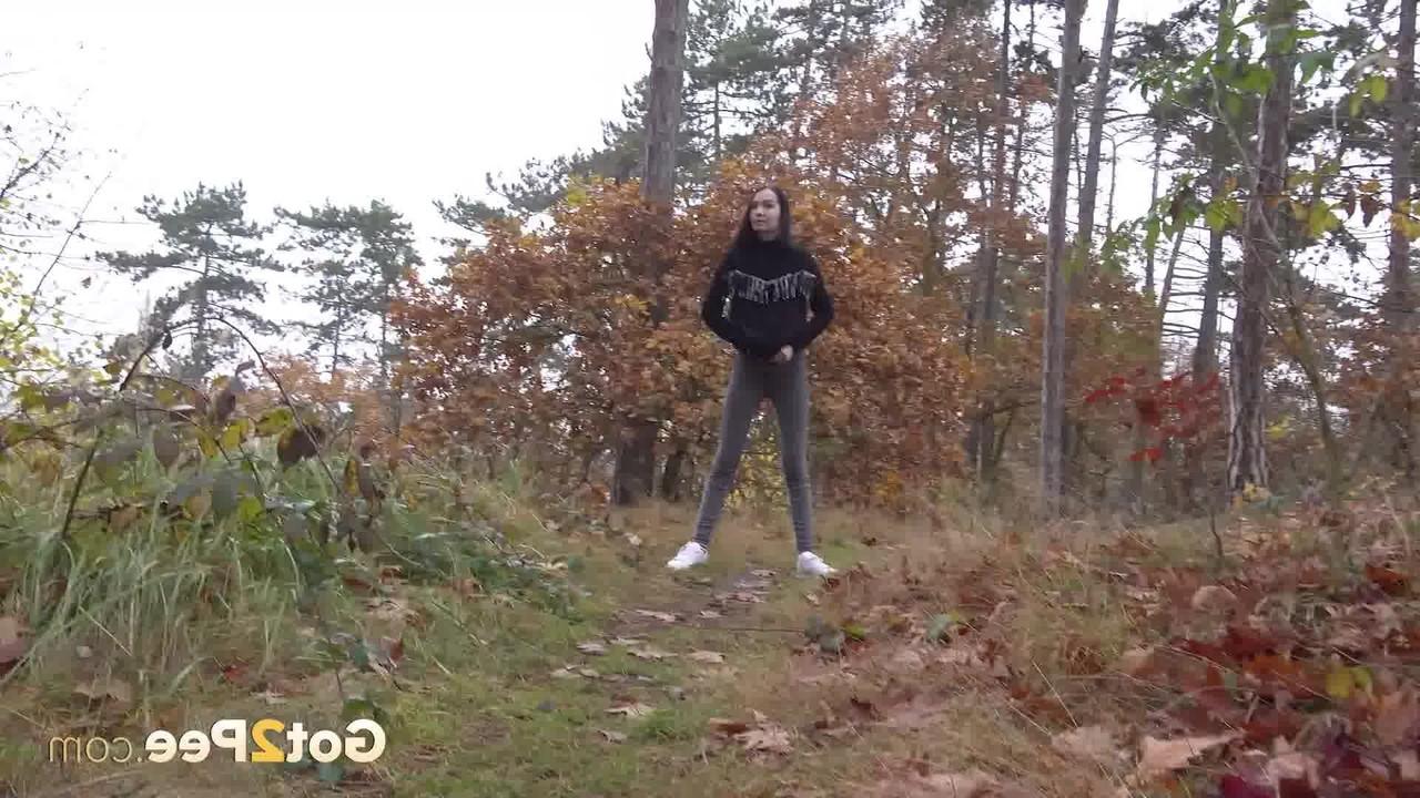 14P Bekleidetes Mädchen zieht ihre Hose herunter, um auf einem Waldweg zu pinkeln
