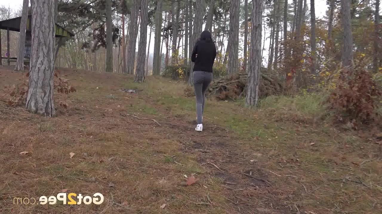 14P Bekleidetes Mädchen zieht ihre Hose herunter, um auf einem Waldweg zu pinkeln