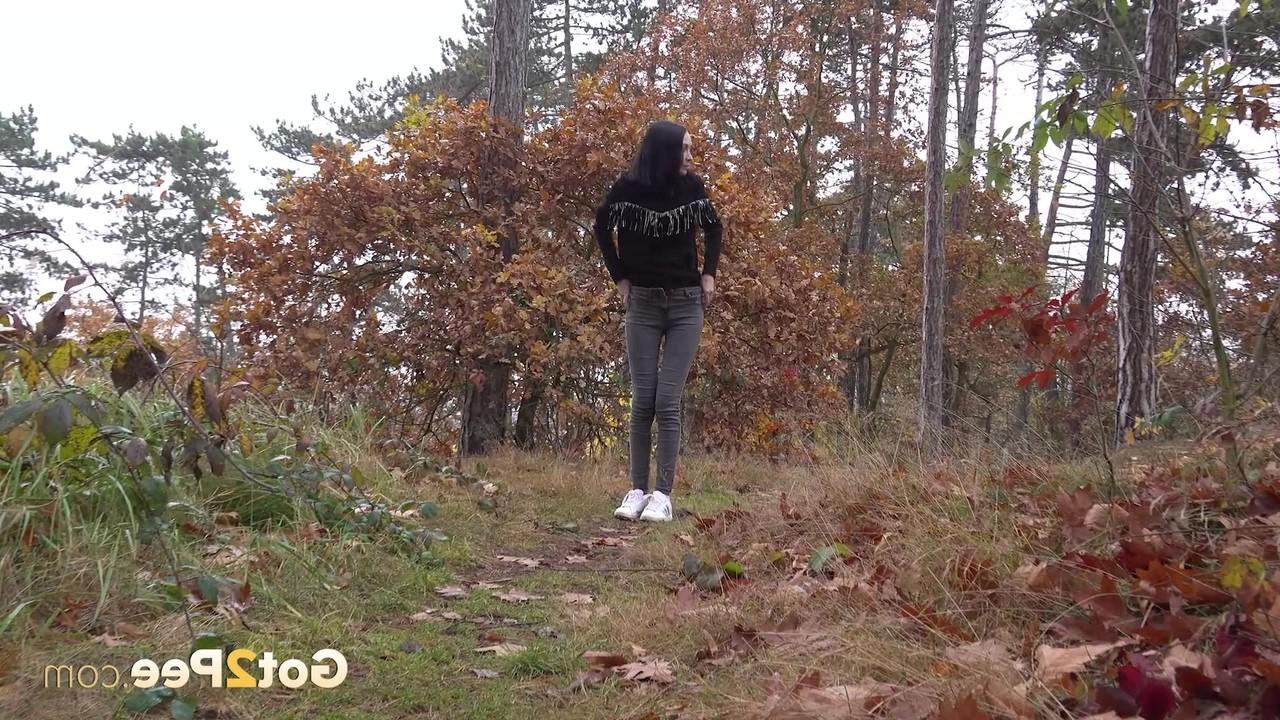 14P Bekleidetes Mädchen zieht ihre Hose herunter, um auf einem Waldweg zu pinkeln