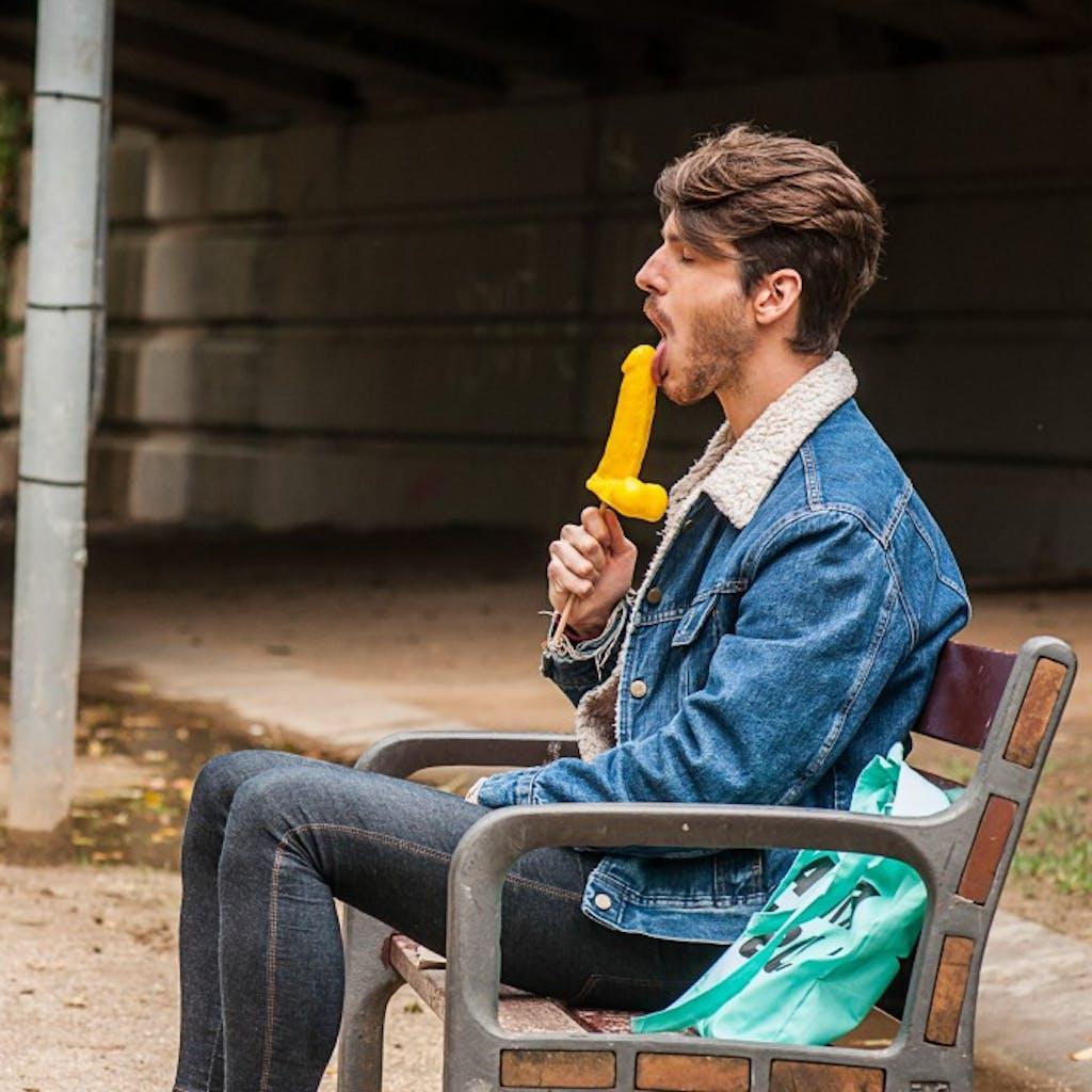 12P Gay brunette Victor A erotically sucks a sex toy lollipop on a public bench