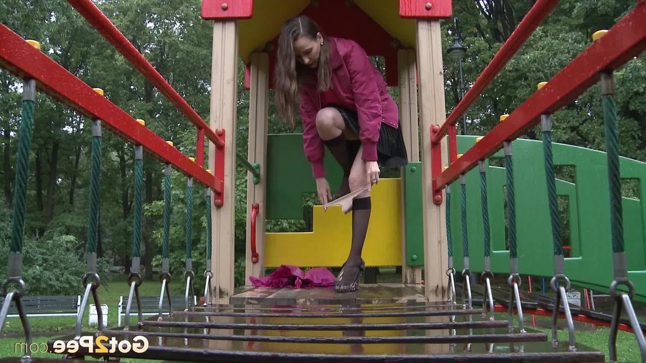 15P A simpática garota Oksana se agacha para mijar no equipamento do playground em um parque público