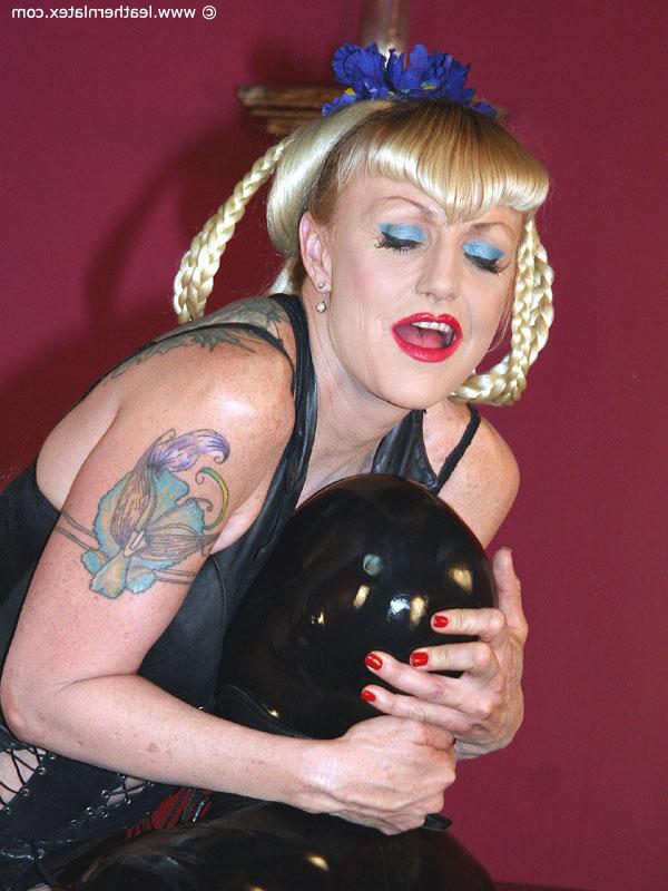 16P Tattooed blonde dominates a latex attired male slave in a dungeon