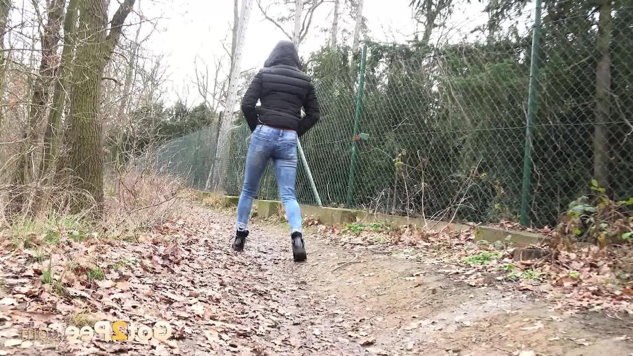 15P A garota branca Lilly puxa jeans rasgados para fazer xixi nas folhas ao lado de um caminho