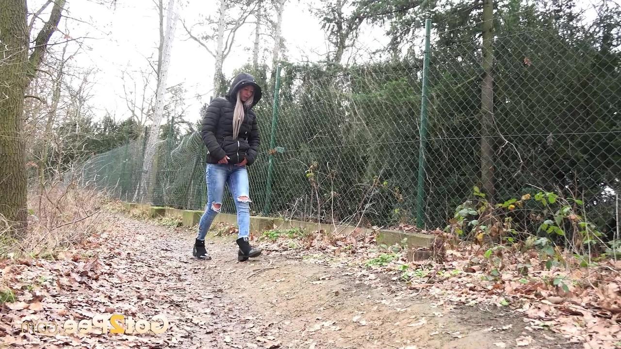 15P A garota branca Lilly puxa jeans rasgados para fazer xixi nas folhas ao lado de um caminho