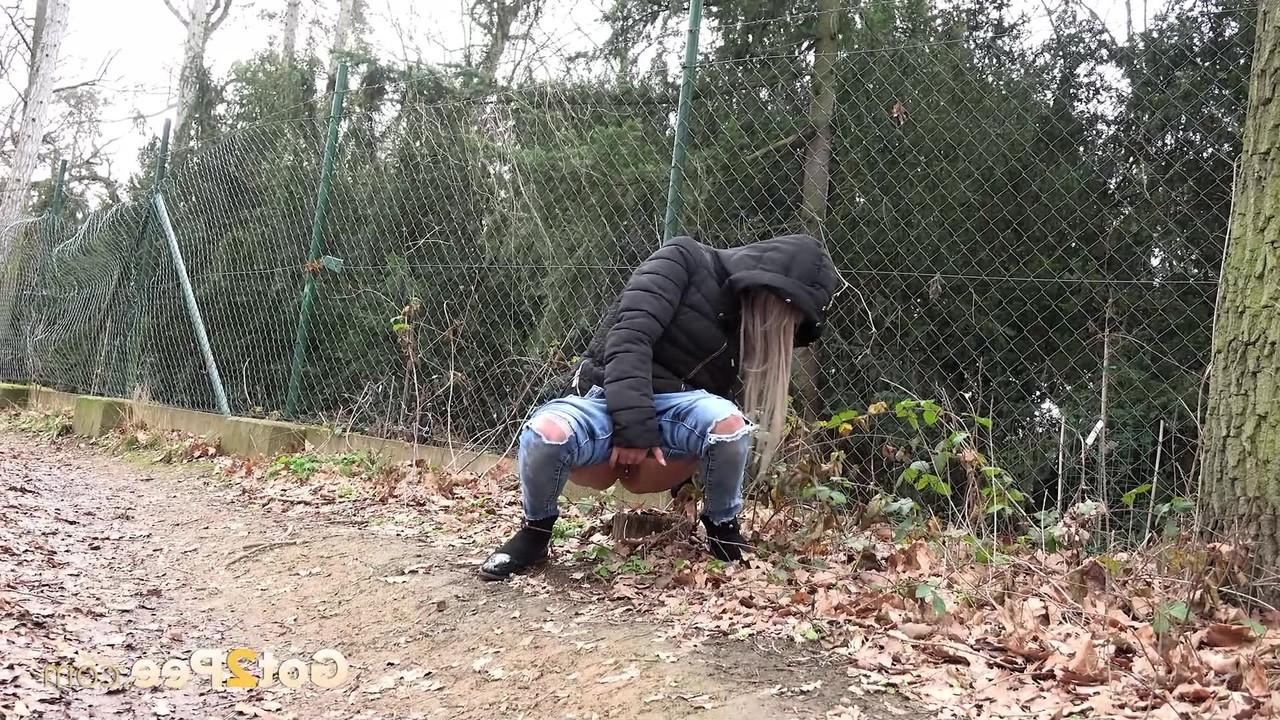 15P A garota branca Lilly puxa jeans rasgados para fazer xixi nas folhas ao lado de um caminho