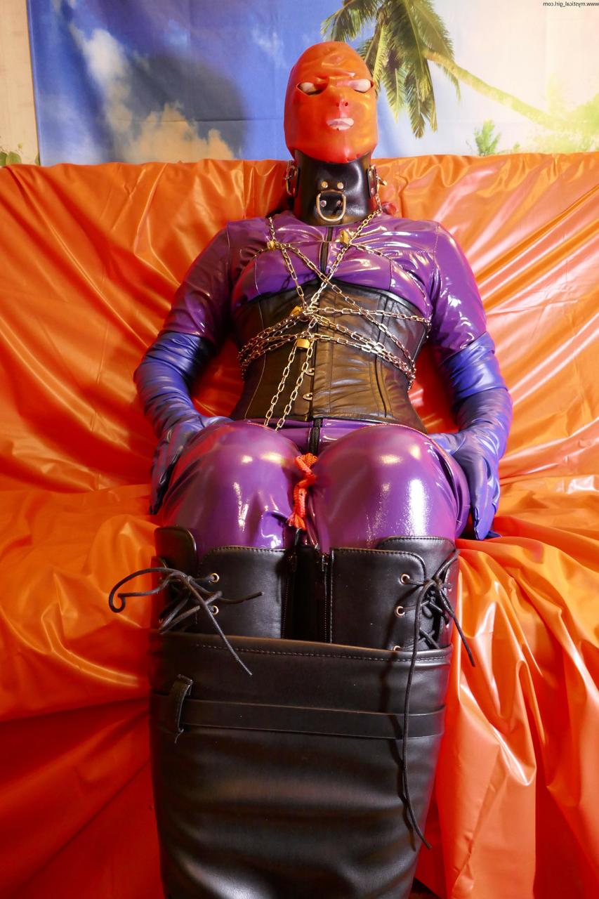 16P Caucasian fetish model is draped in chain while wearing latex attire