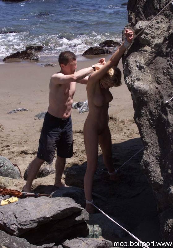 17P A escrava madura nua Sadie Belle fica amarrada a uma pedra enorme na praia