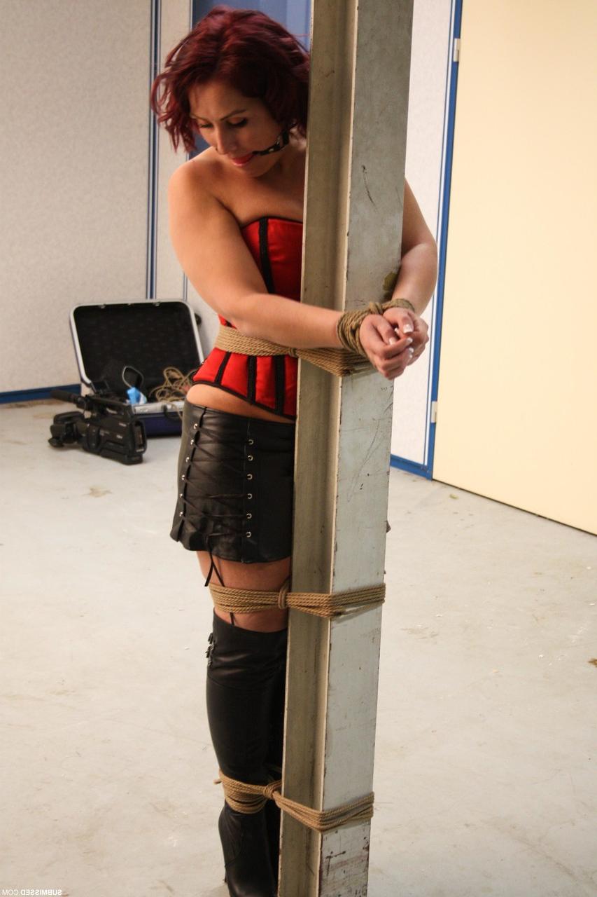 20P Corseted babe in boots Rani gets bound to a pole while ball gagged