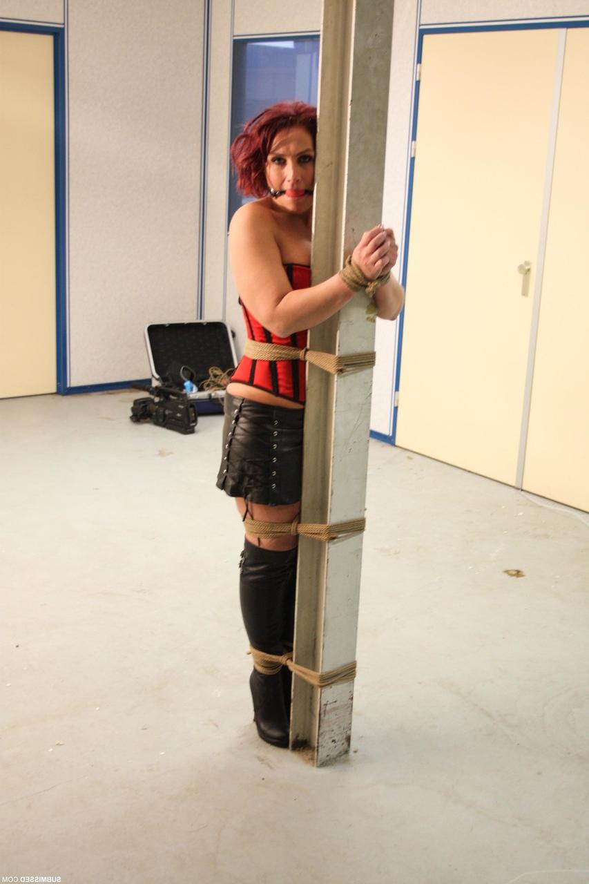 20P Corseted babe in boots Rani gets bound to a pole while ball gagged