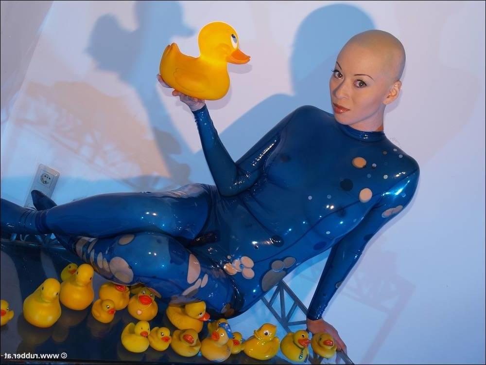 16P Bald female models rubber attire during a solo engagement
