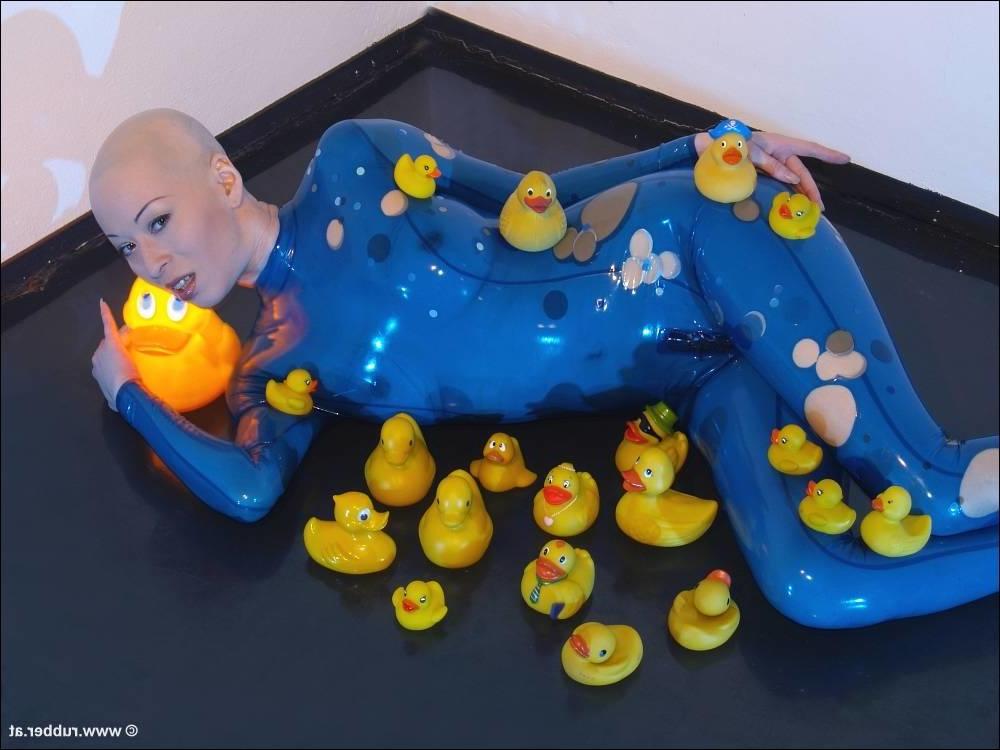 16P Bald female models rubber attire during a solo engagement