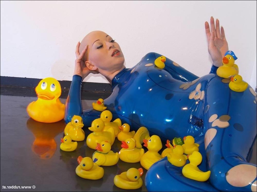 16P Bald female models rubber attire during a solo engagement