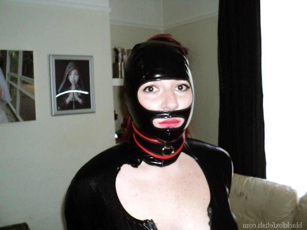 16P Redheaded slave is fitted with a hood and ball gag in black latex clothing
