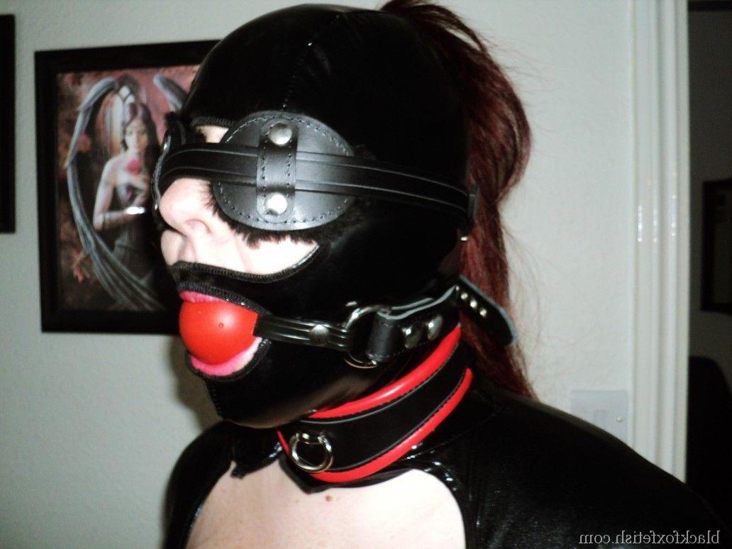 16P Redheaded slave is fitted with a hood and ball gag in black latex clothing