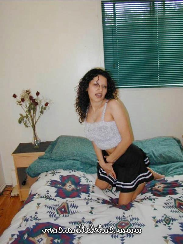 15P Une jolie fille latina découvre ses seins naturels en s'agenouillant sur un lit.