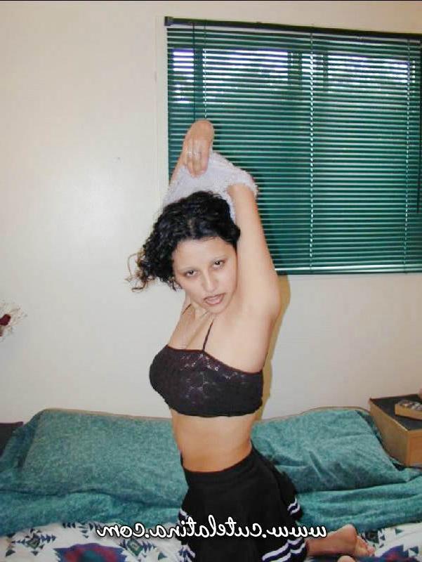 15P Une jolie fille latina découvre ses seins naturels en s'agenouillant sur un lit.