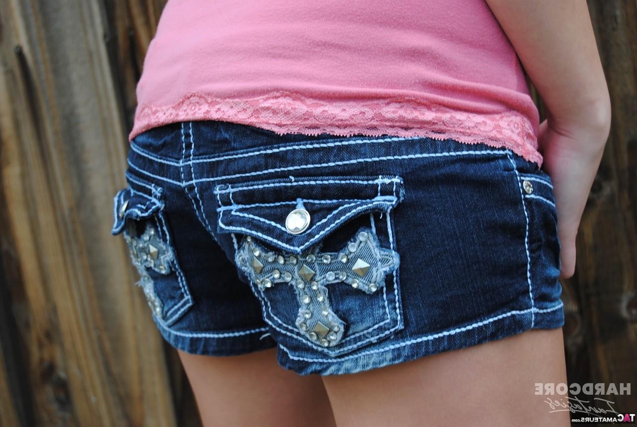 16P Das Amateurmädchen Heavenly Smut posiert in Jeansshorts in der Nähe eines Hinterhofzauns