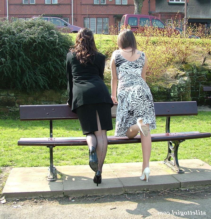 16P Clothed females admire each other high heeled shoes on a park bench