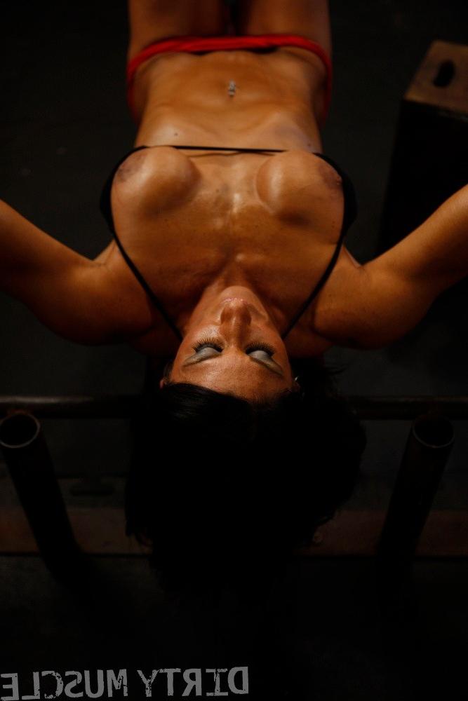 17P Brunette bodybuilder pauses to flex her muscles while pumping iron on a bench
