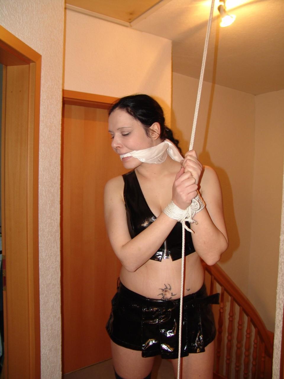 16P Brunette chick is tied up with ropes in black latex apparel and long boots