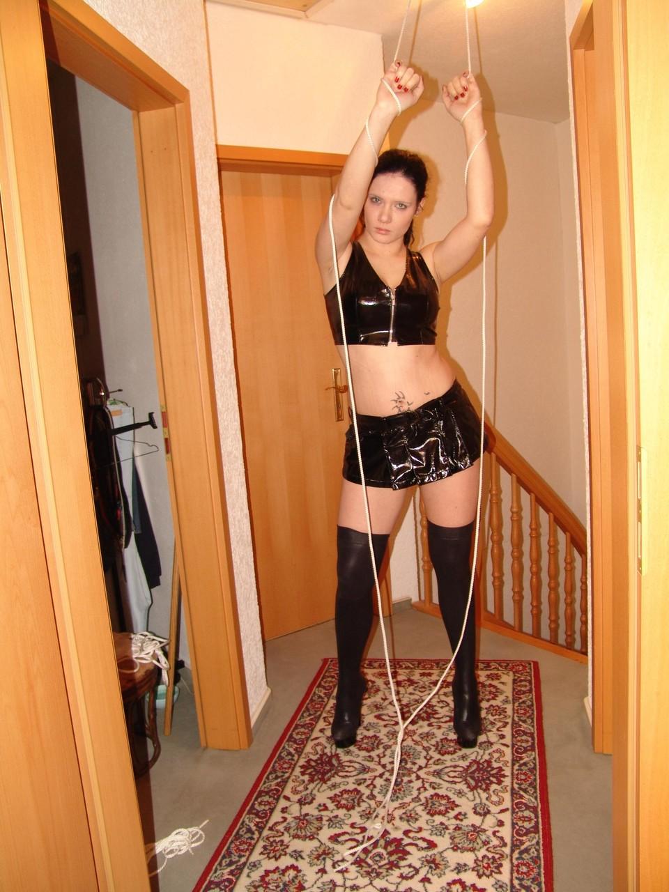 16P Brunette chick is tied up with ropes in black latex apparel and long boots
