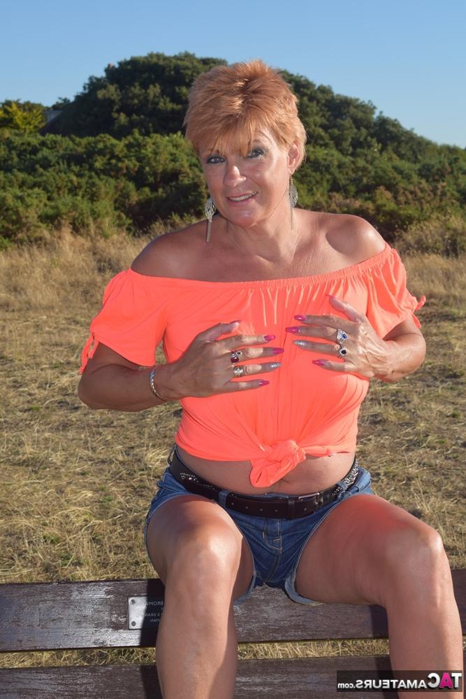 20P La madura pelirroja Dimonty muestra sus tetas en un banco de un campo rural