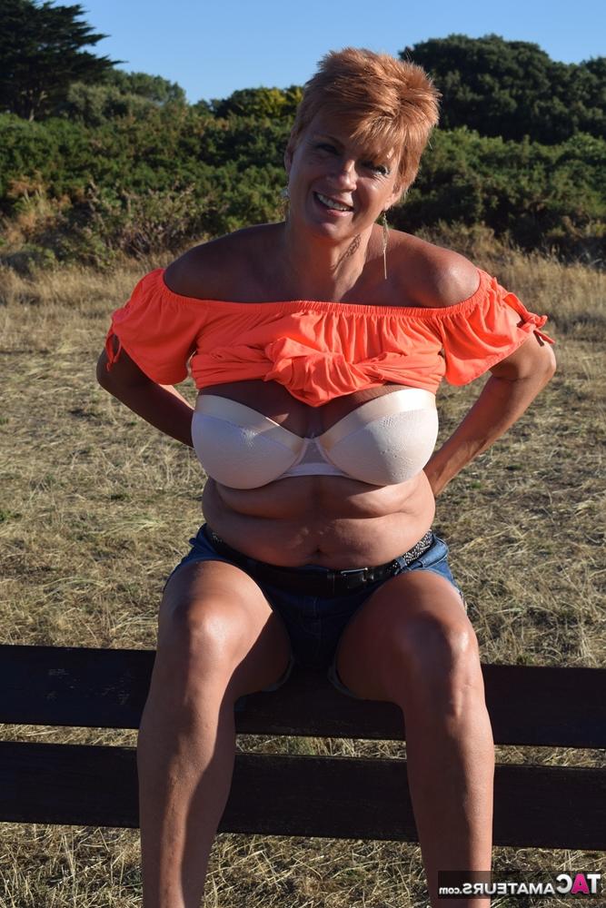 20P La madura pelirroja Dimonty muestra sus tetas en un banco de un campo rural