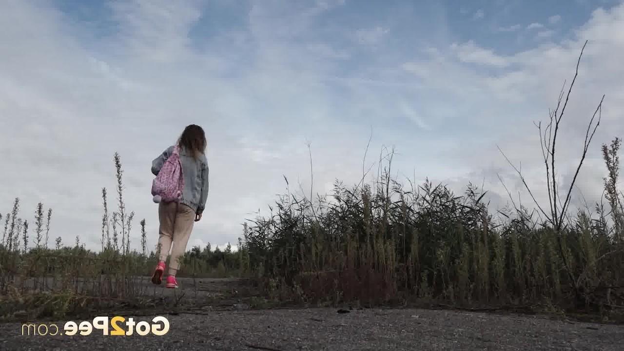 15P Rita, une fille blanche, baisse son sweat pour faire pipi à côté de longues herbes.