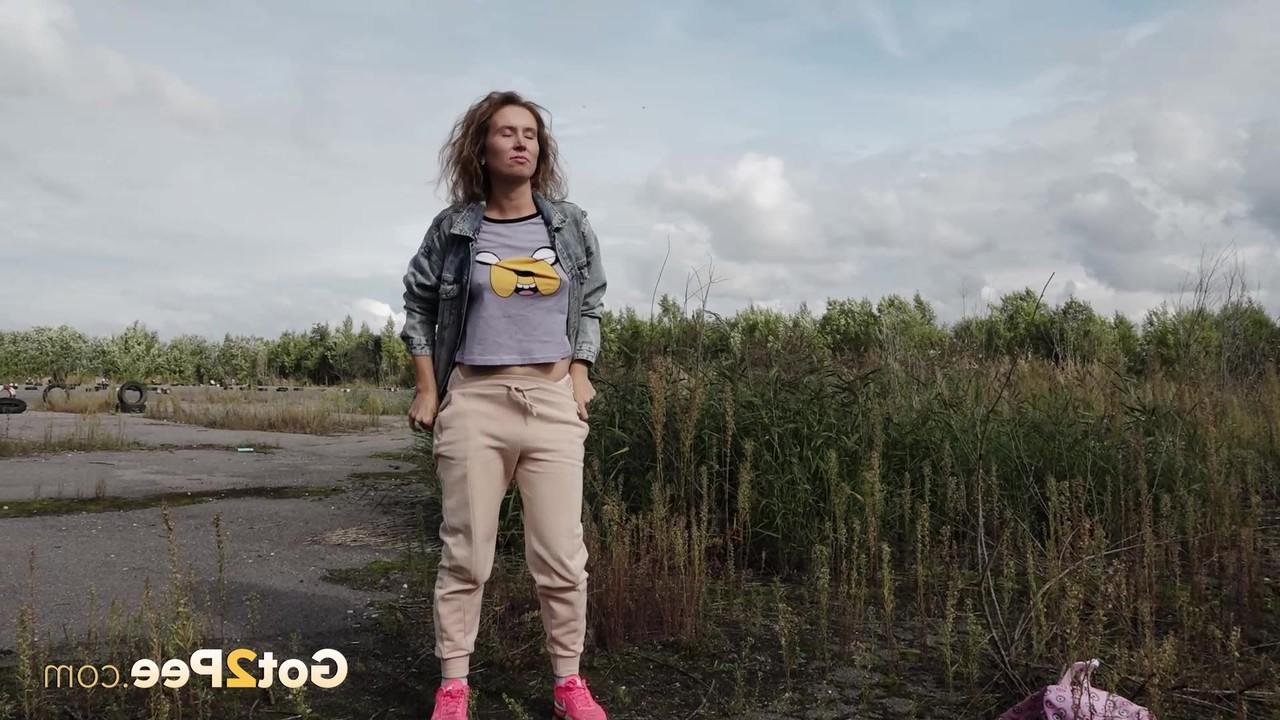 15P Rita, une fille blanche, baisse son sweat pour faire pipi à côté de longues herbes.