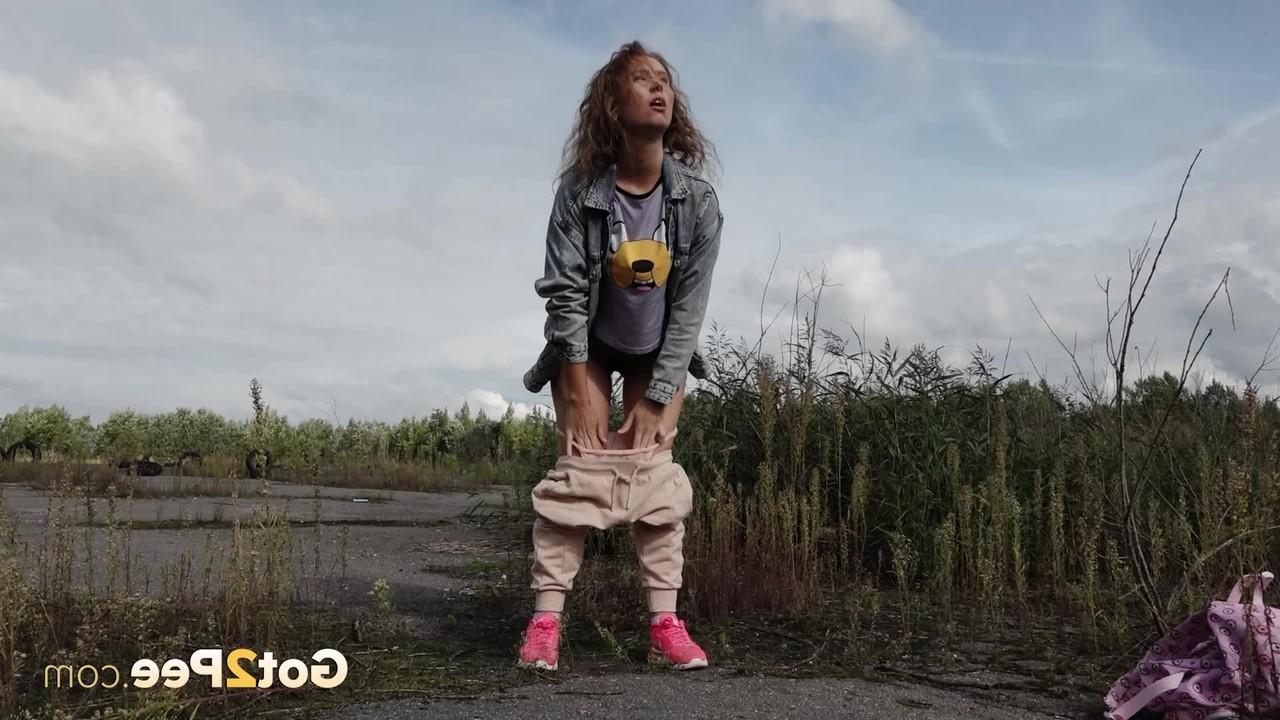 15P Rita, une fille blanche, baisse son sweat pour faire pipi à côté de longues herbes.