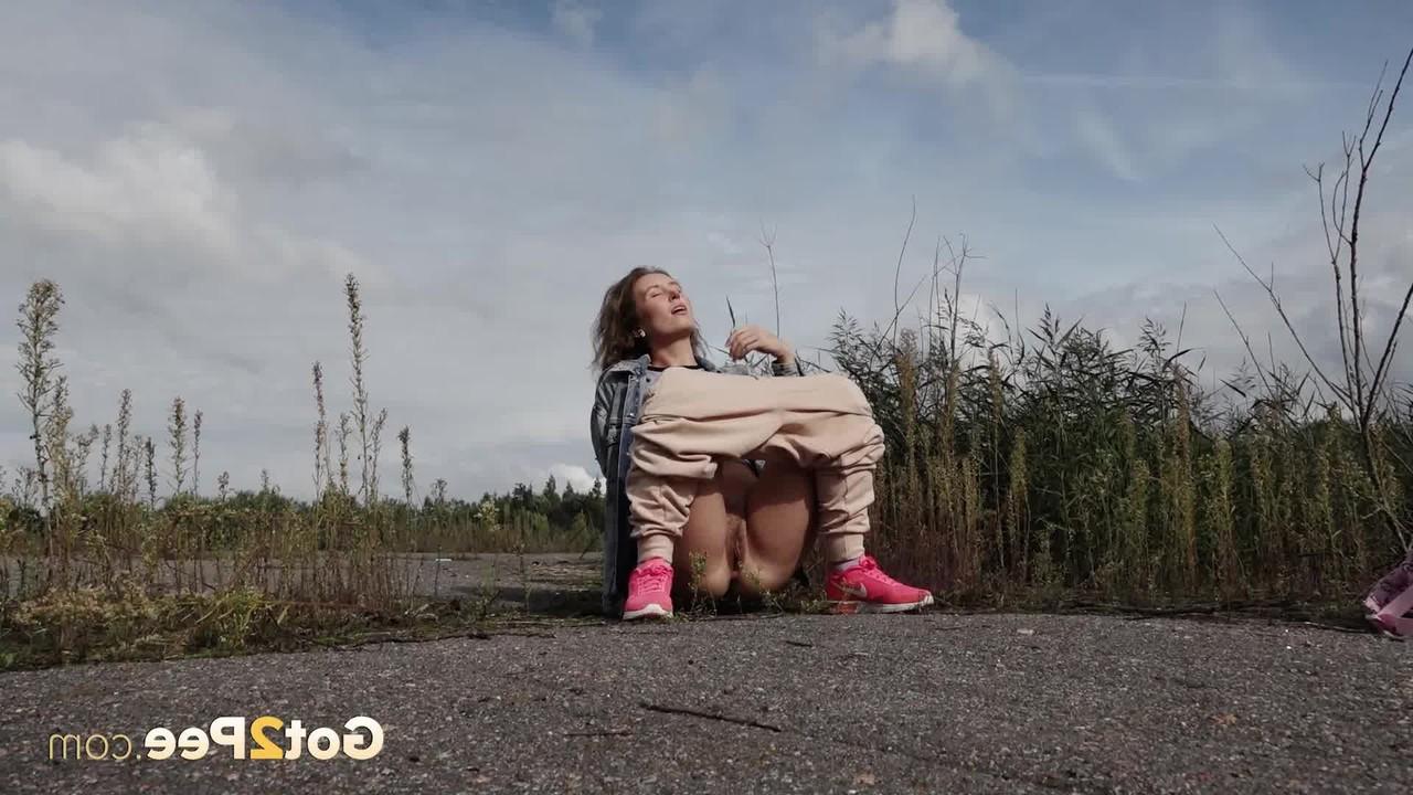 15P Rita, une fille blanche, baisse son sweat pour faire pipi à côté de longues herbes.