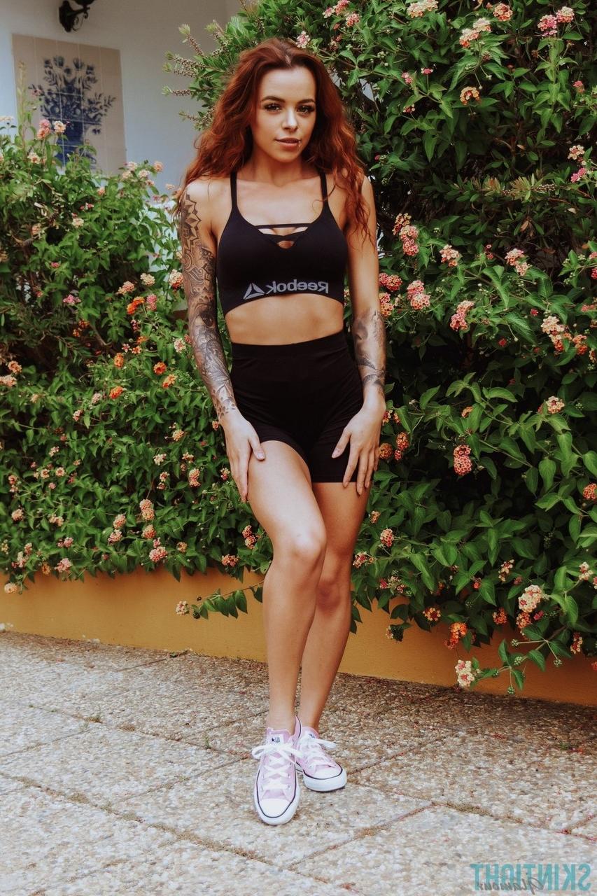 12P La rousse tatouée Mia Stryker enlève ses vêtements de sport devant des buissons en fleurs
