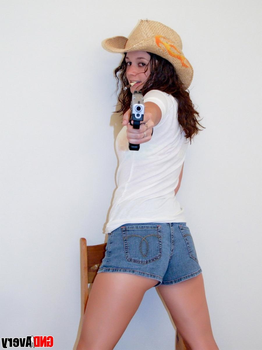 12P Encantadora adolescente morena empuña una pistola mientras se desnuda en calzado