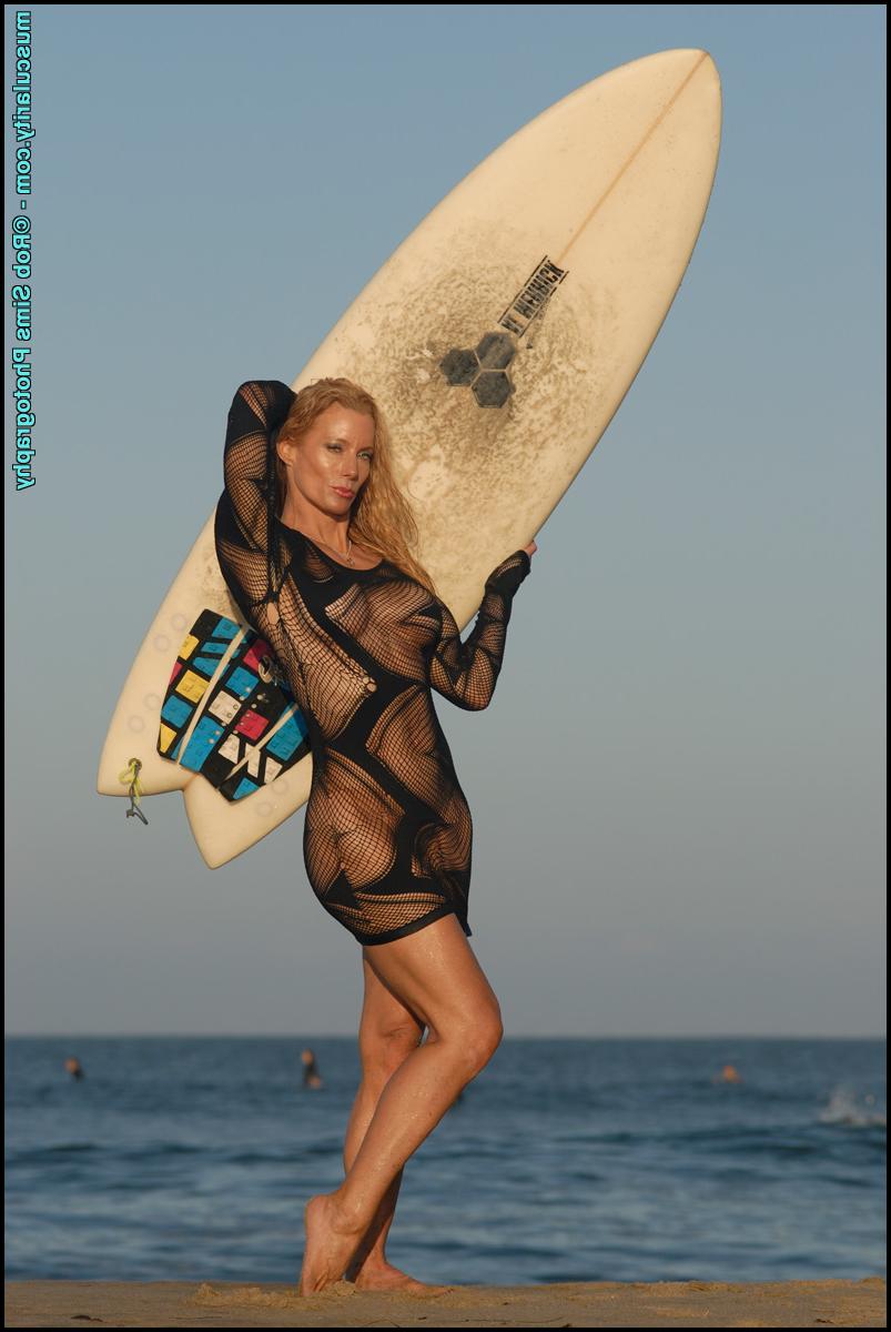 15P La modelo de fitness Rebecca Ewing toma una tabla de surf mientras modela en la playa