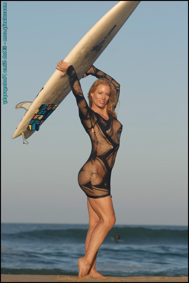 15P La modelo de fitness Rebecca Ewing toma una tabla de surf mientras modela en la playa