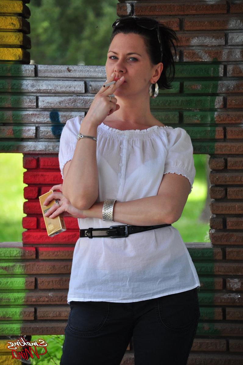 15P Fully clothed brunette Mina smokes a cigarette in front of a brick wall
